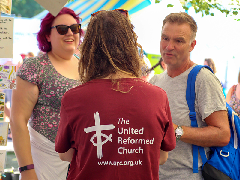 A URC volunteer at Greenbelt speaking to two festival goers